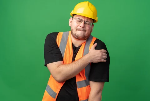 Homme portant un casque de chantier et semblant avoir mal à l'épaule