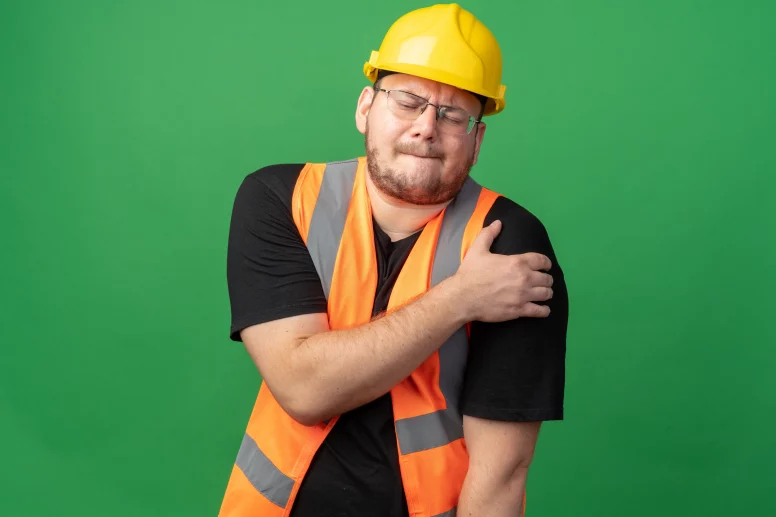 Homme portant un casque de chantier et semblant avoir mal à l'épaule
